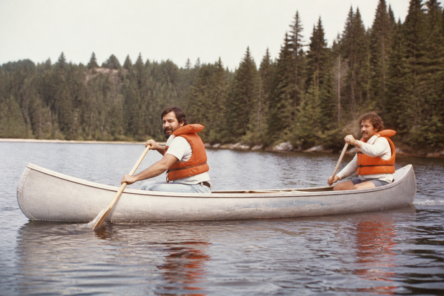 Two men in an aluminum canoe wearing bulky orange life vests